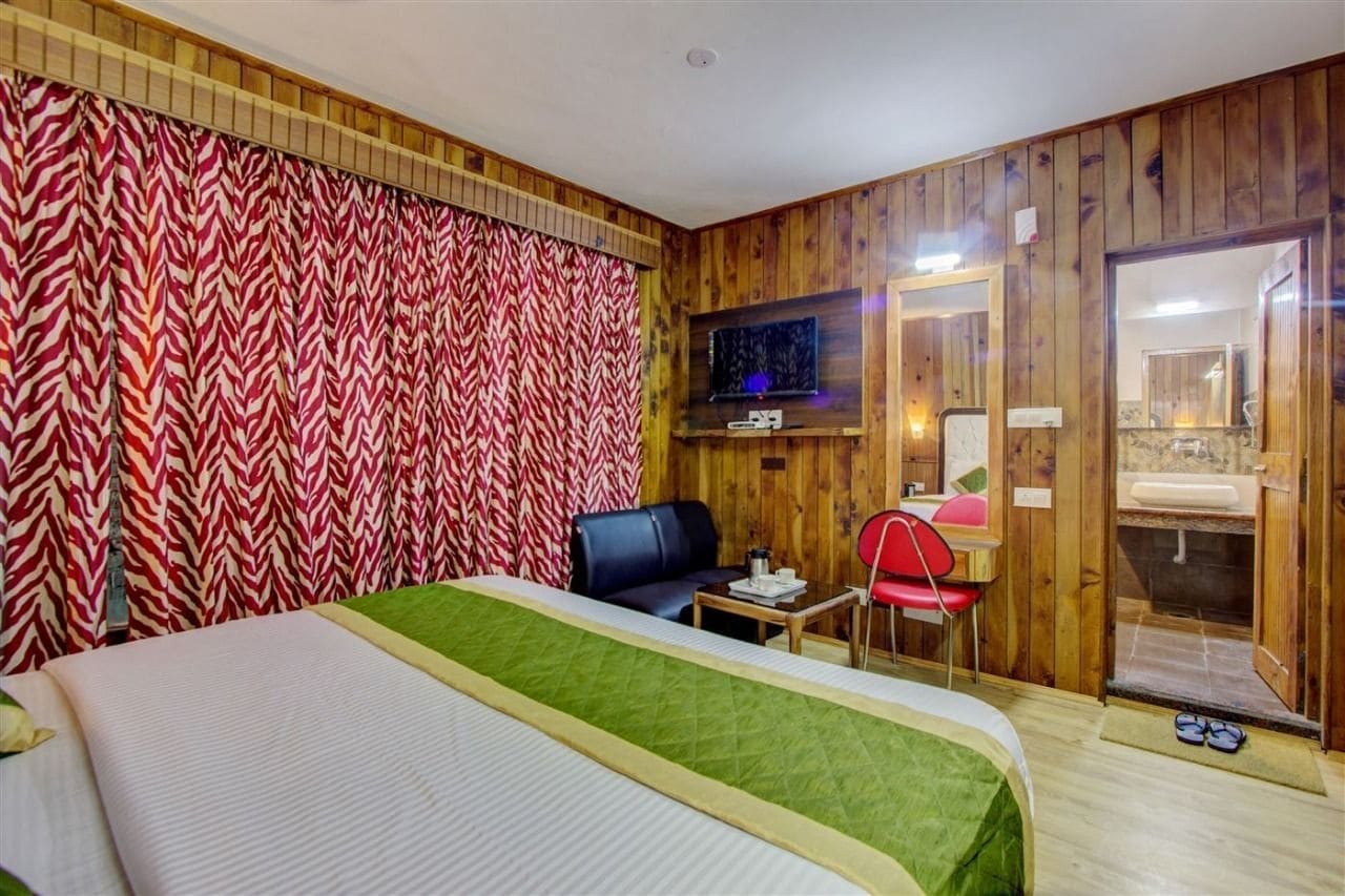 A hotel room with a bed, a desk, a chair, a television, and a bathroom visible through an open door.