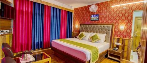 Habitación de hotel con una cama grande, televisión, mesita de noche, una silla y una mesa de centro.