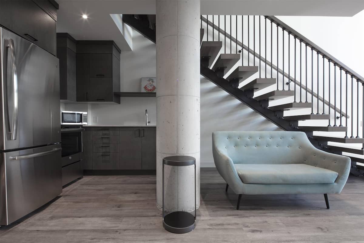 A modern kitchen with stainless steel appliances, a round trash bin, and a light blue sofa.
