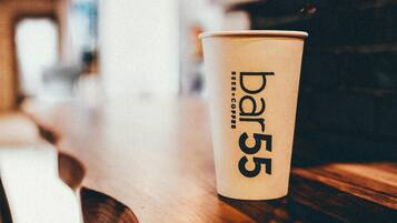 A bar stool with a paper cup labeled 'bar55' on a wooden counter.
