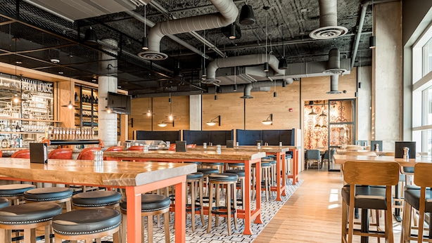 A modern bar area with high ceilings, exposed ductwork, and a variety of seating options including bar stools and tables. - Canvas Moncton, Tapestry Collection by Hilton (Moncton)