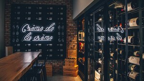 A bar area with a neon sign, wooden crates, and shelves of bottles. - Canvas Moncton, Tapestry Collection by Hilton (Moncton)