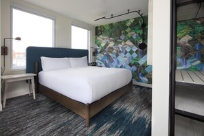 A bedroom with a bed, a desk, a window, and a wall with a geometric pattern. - Canvas Moncton, Tapestry Collection by Hilton (Moncton)