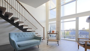 A spacious room with a light blue sofa, a wooden chair, a small table, and a staircase with a wooden handrail. - Canvas Moncton, Tapestry Collection by Hilton (Moncton)