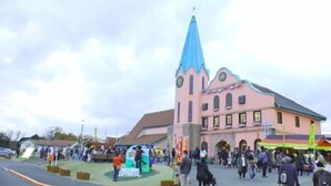 A building with a pink facade and a blue spire, surrounded by a crowd. - Hotel Swan Lake Nagara (Ichihara)
