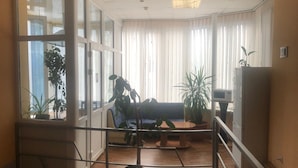A spacious living area with a large window, a sofa, a coffee table, and several potted plants. - Hotel LaMa 2 (Kyiv)