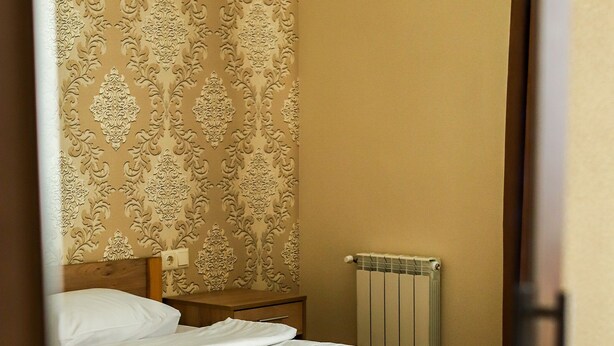 A neatly made bed with white linens and folded towels, a wooden headboard, and a radiator on the wall. - Hotel LaMa 2 (Kyiv)