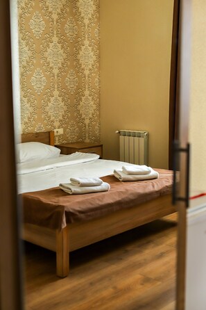 Un lit bien fait, avec du linge de lit blanc et des serviettes pliées, une tête de lit en bois et un radiateur au mur.