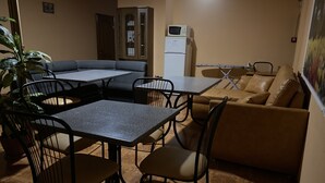 A cozy living room with a sofa, two dining tables, and chairs. There is a cabinet and a refrigerator in the background. - Hotel LaMa 2 (Kyiv)