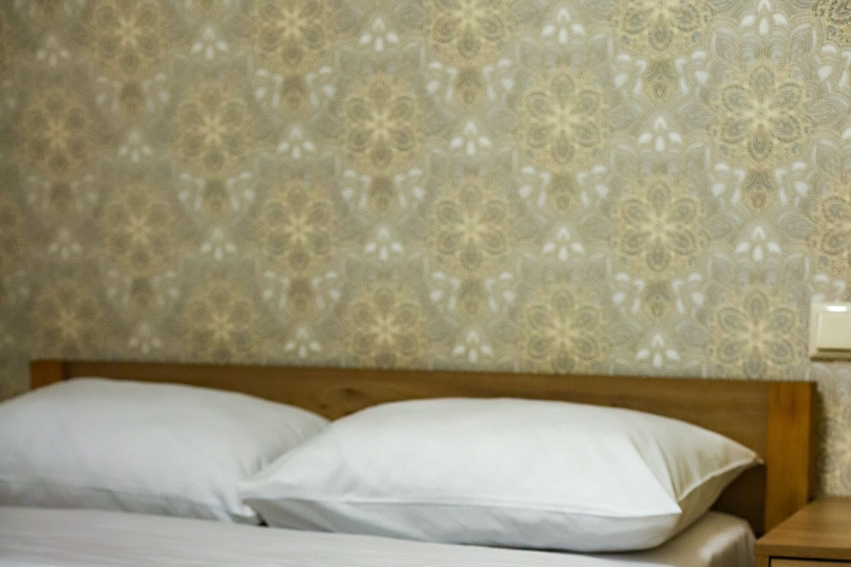 A single bed with white linens in a room with patterned wallpaper and wooden flooring.