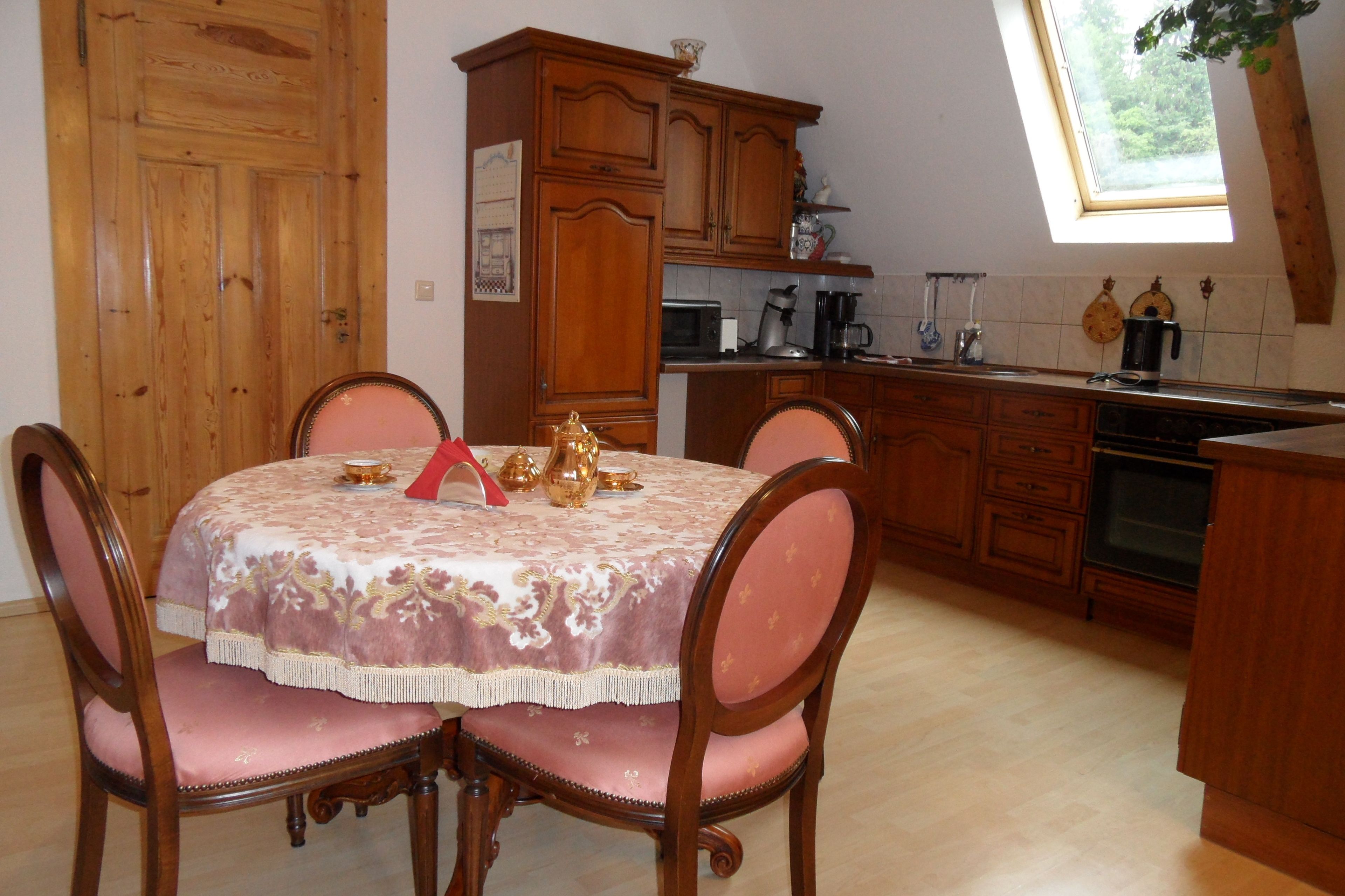 A dining area with a table set for four, wooden cabinets, and a window with a view of greenery.