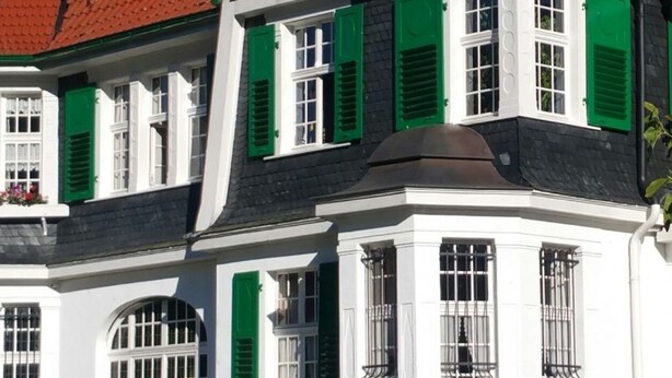 A traditional half-timbered house with a red tiled roof, green shutters, and a statue in front.