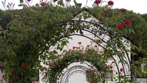 A garden pathway leading to a white building with a metal archway covered in red roses.