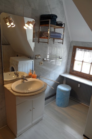 Un baño con lavamanos, espejo, toallero y ventana.