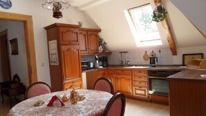 A kitchen with wooden cabinets, a dining table with a floral tablecloth, and a window with a plant.