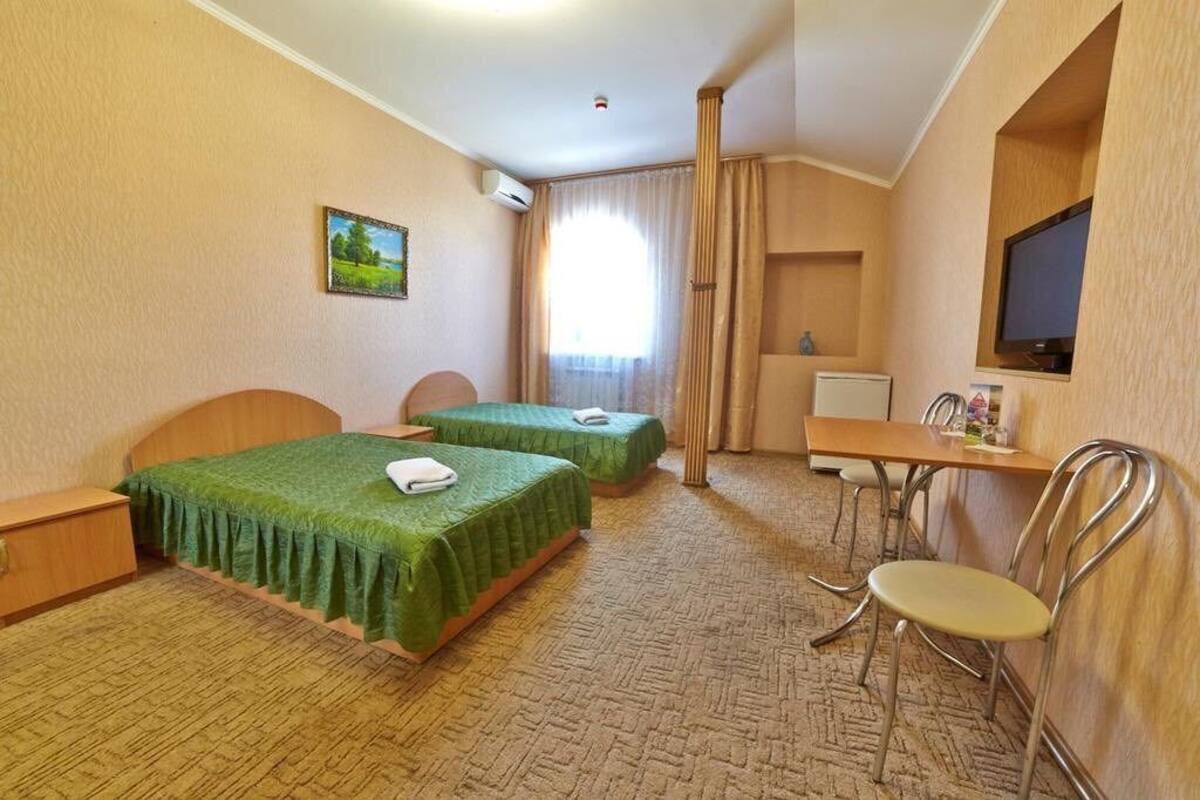Hotellihuone, jossa on kaksi erillistä sänkyä, työpöytä tuolilla, televisio ja ikkuna, jossa on verhot.