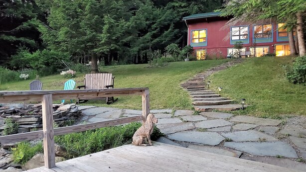 Une terrasse en bois avec un chemin de pierre menant à une maison à l’extérieur rouge et aux bordures bleues.
