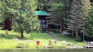 Un chalet au bord du lac, doté d’un toit végétalisé, entouré d’arbres et d’une pelouse aménagée avec des sièges d’extérieur.