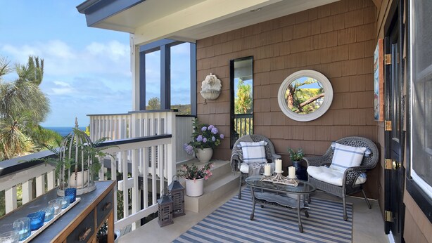 A balcony with a railing, a seating area with two chairs and a table, a potted plant, and a decorative mirror. - Serenity in the Hills - A Chic Coastal Apartment with Balcony & Ocean Glimpses (Laguna Beach)