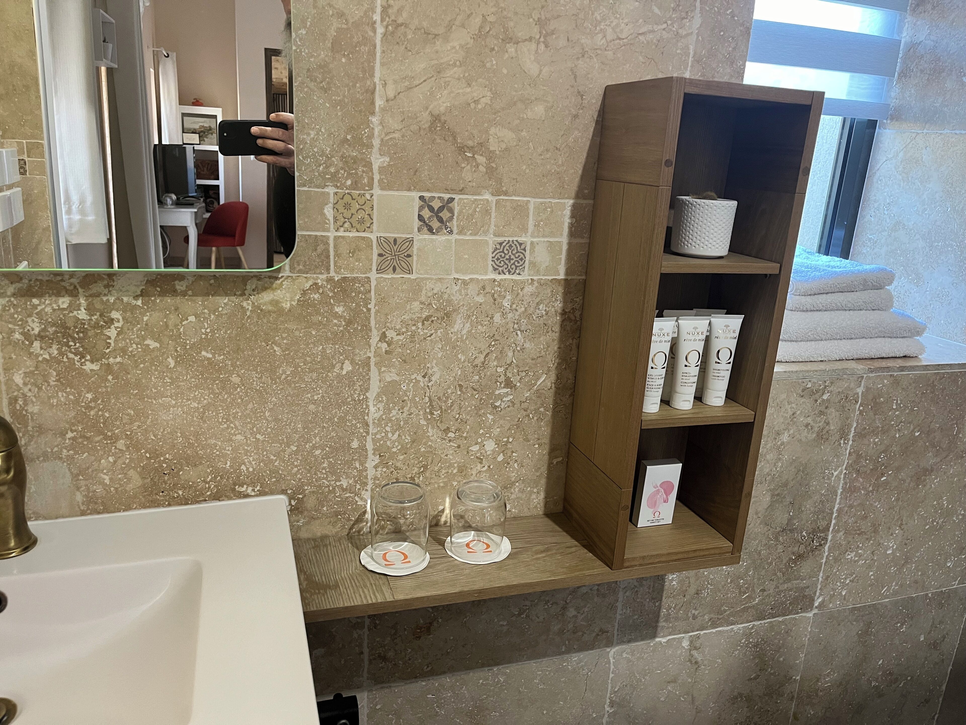 Een badkamer met een marmeren spatwand, een houten plank met toiletartikelen, en een spiegel die de kamer weerspiegelt.