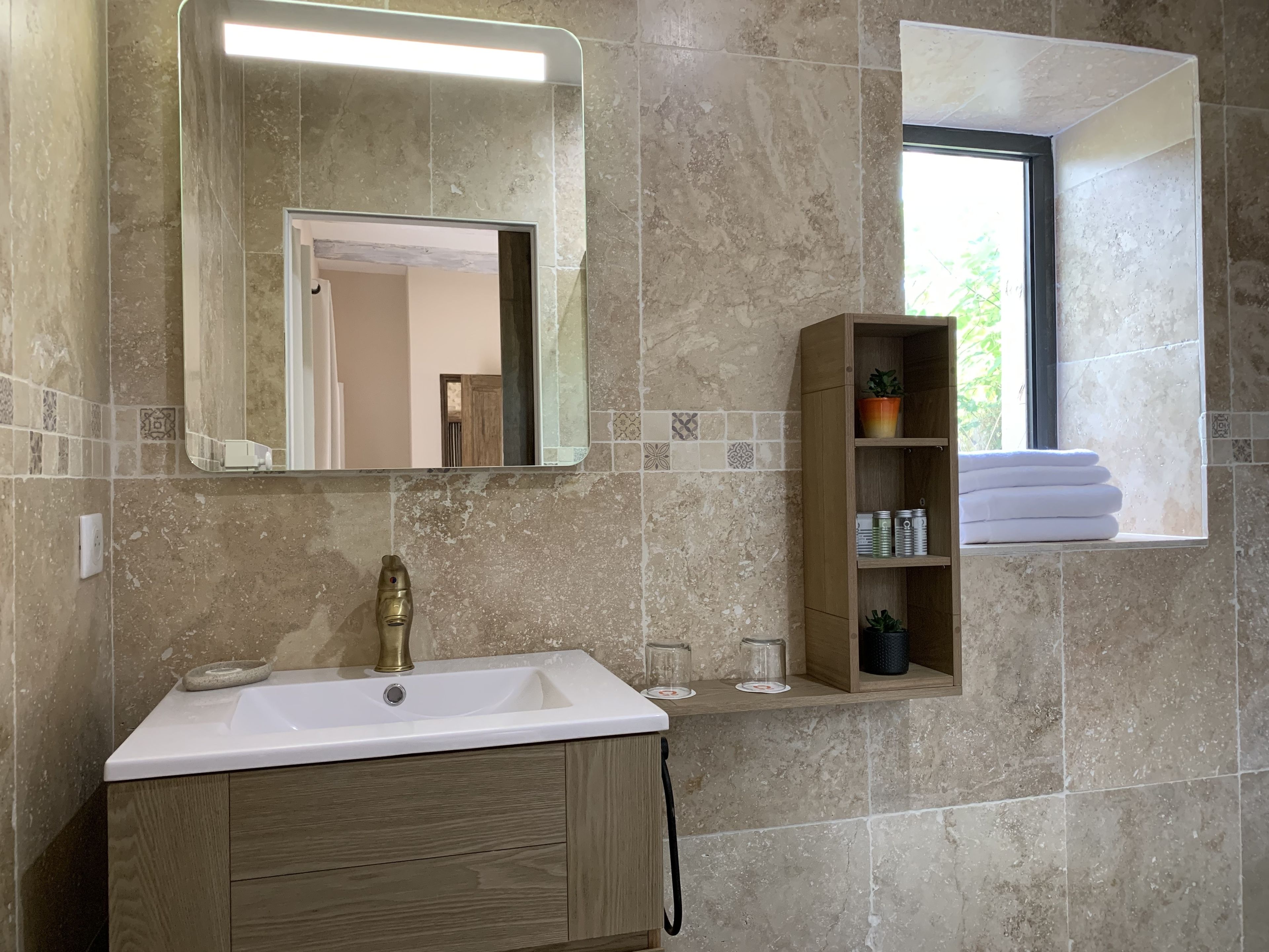 Casa de banho com lavatório, espelho e prateleira com toalhas e artigos de higiene pessoal.