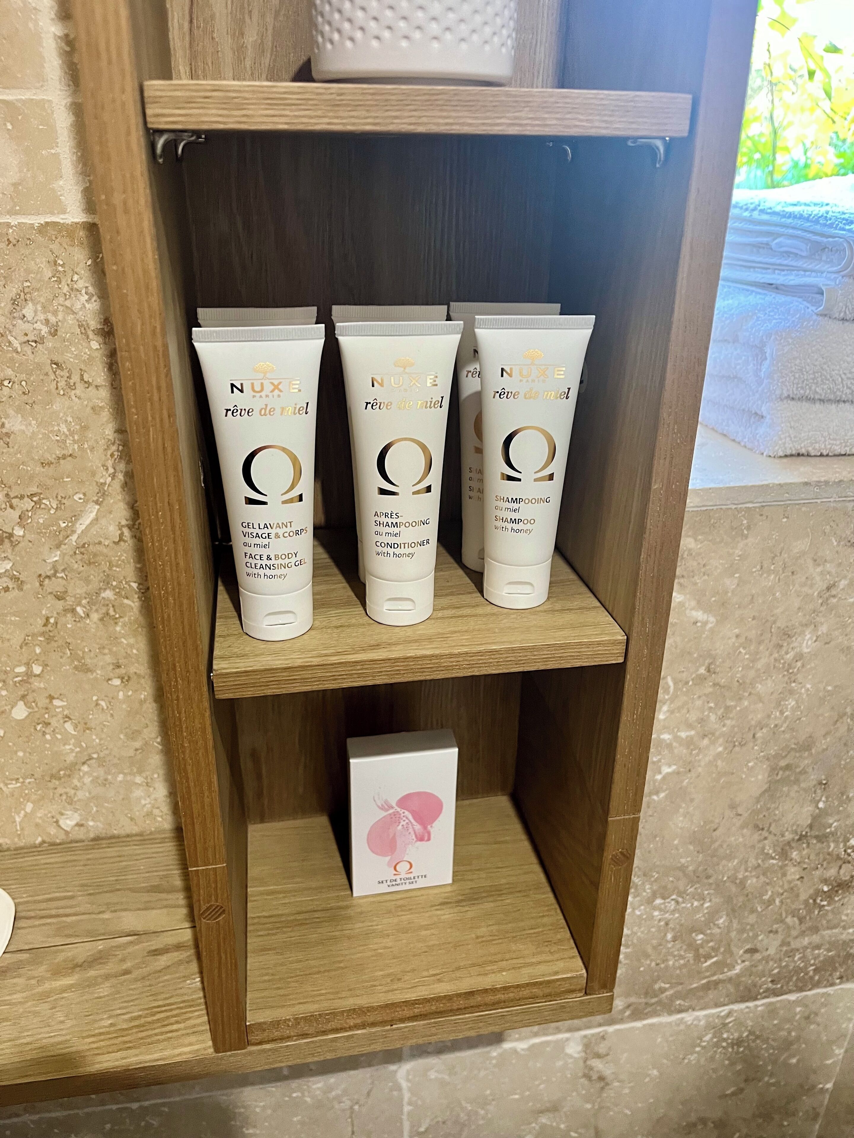 A wooden shelf with three Nuxe Paris skincare products and a small box of Nuxe Paris toiletry set.