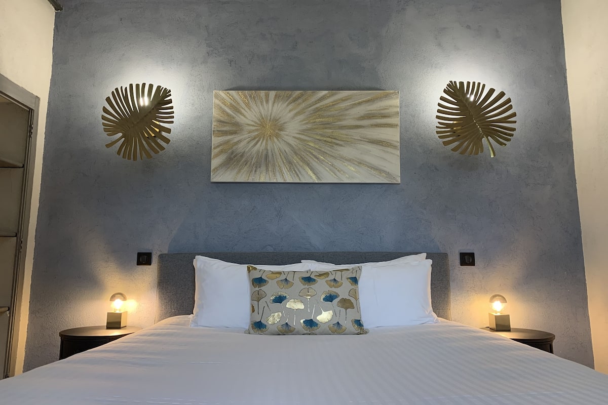 A bedroom with a bed, two wall sconces, a large abstract painting, and decorative wall sconces.