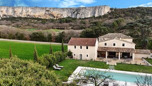 A stone building with a tiled roof, a swimming pool, and a view of a cliff. - Le Mas aux cedres (Lioux)