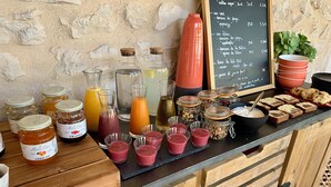 A breakfast bar with various food items and beverages, including jars of jam, bottles of juice, and a chalkboard menu. - Le Mas aux cedres (Lioux)