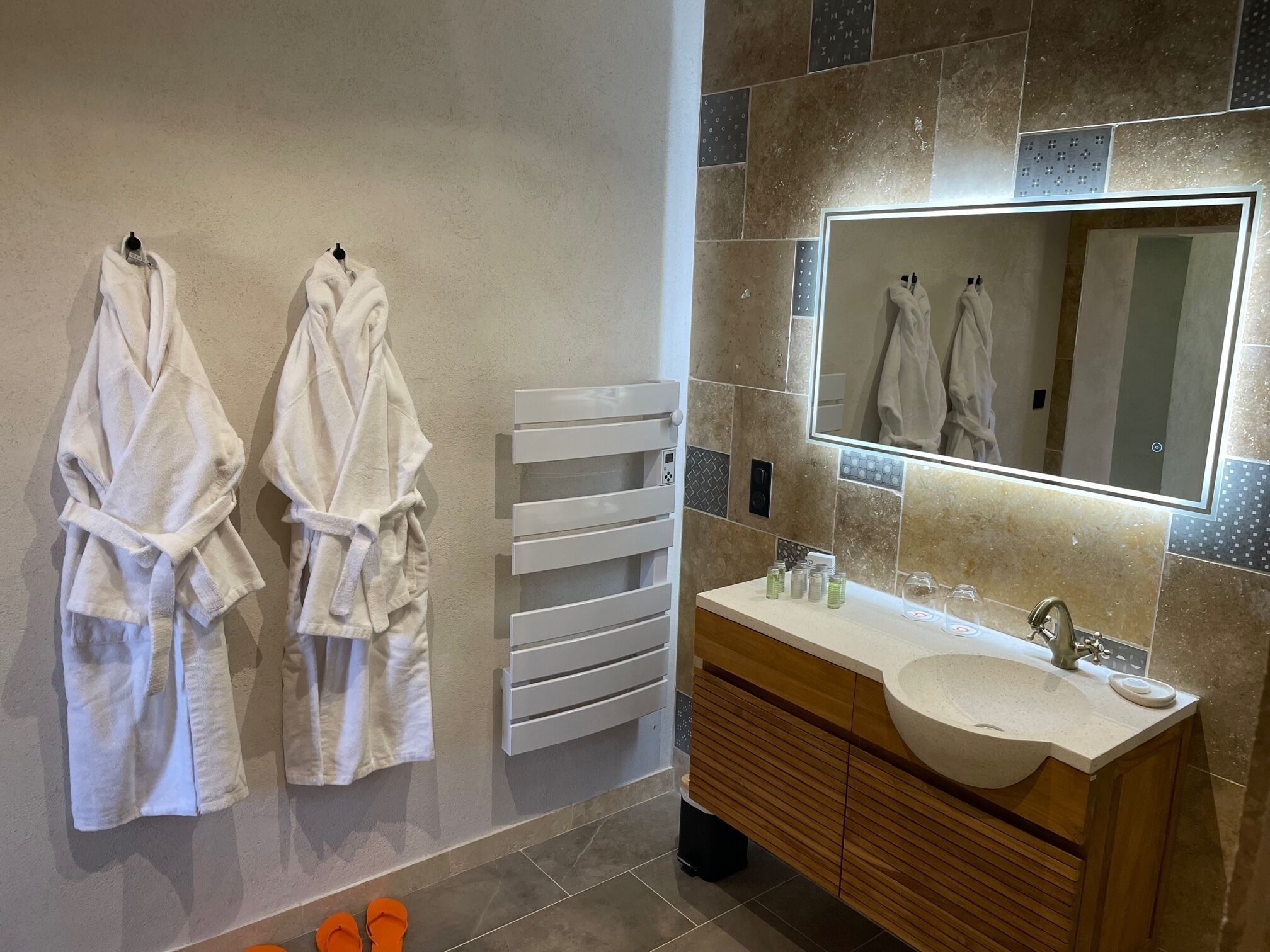 A modern bathroom with two white towels hanging on hooks, a white towel rack, a wooden vanity with a large mirror, and a sink.