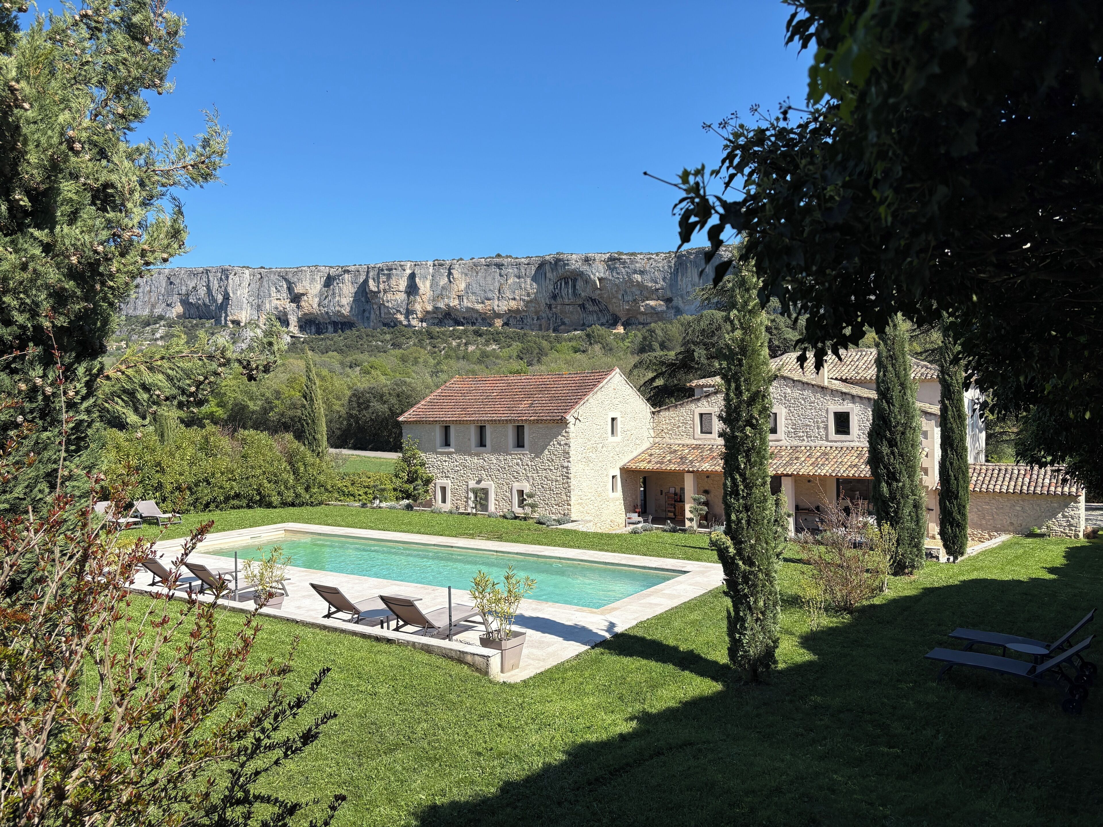 Una casa de piedra con piscina, rodeada de vegetación y un paisaje montañoso.