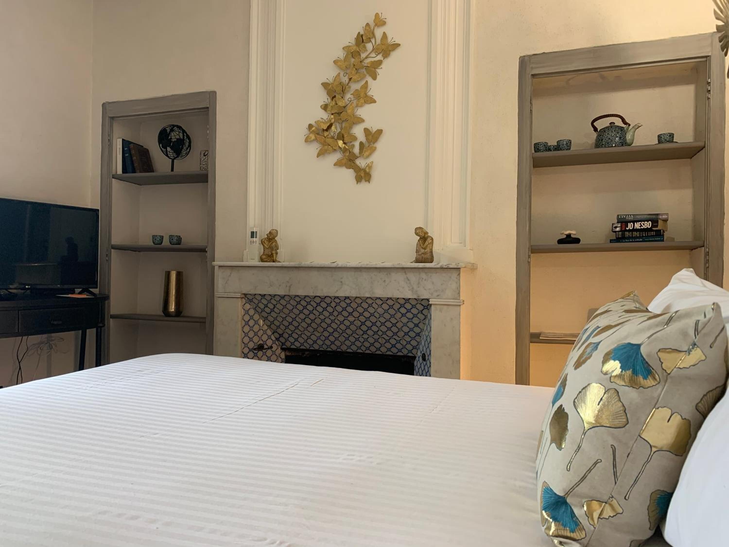 A hotel room with a bed, a television, a fireplace, and shelves with decorative items.