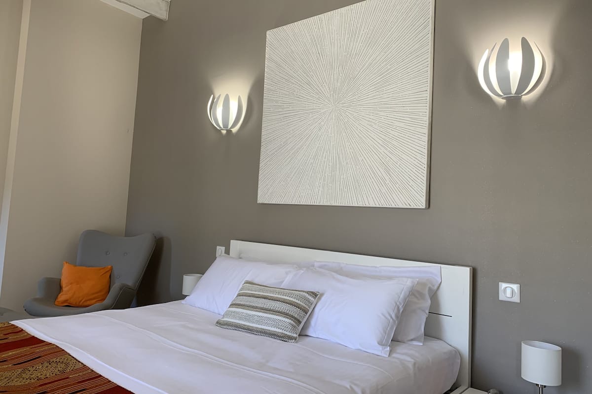 A hotel room with a bed, a gray wall, and two wall-mounted light fixtures.