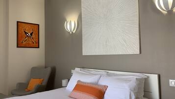 Habitación de hotel con cama, una silla, una obra de arte colgada en la pared y dos apliques.