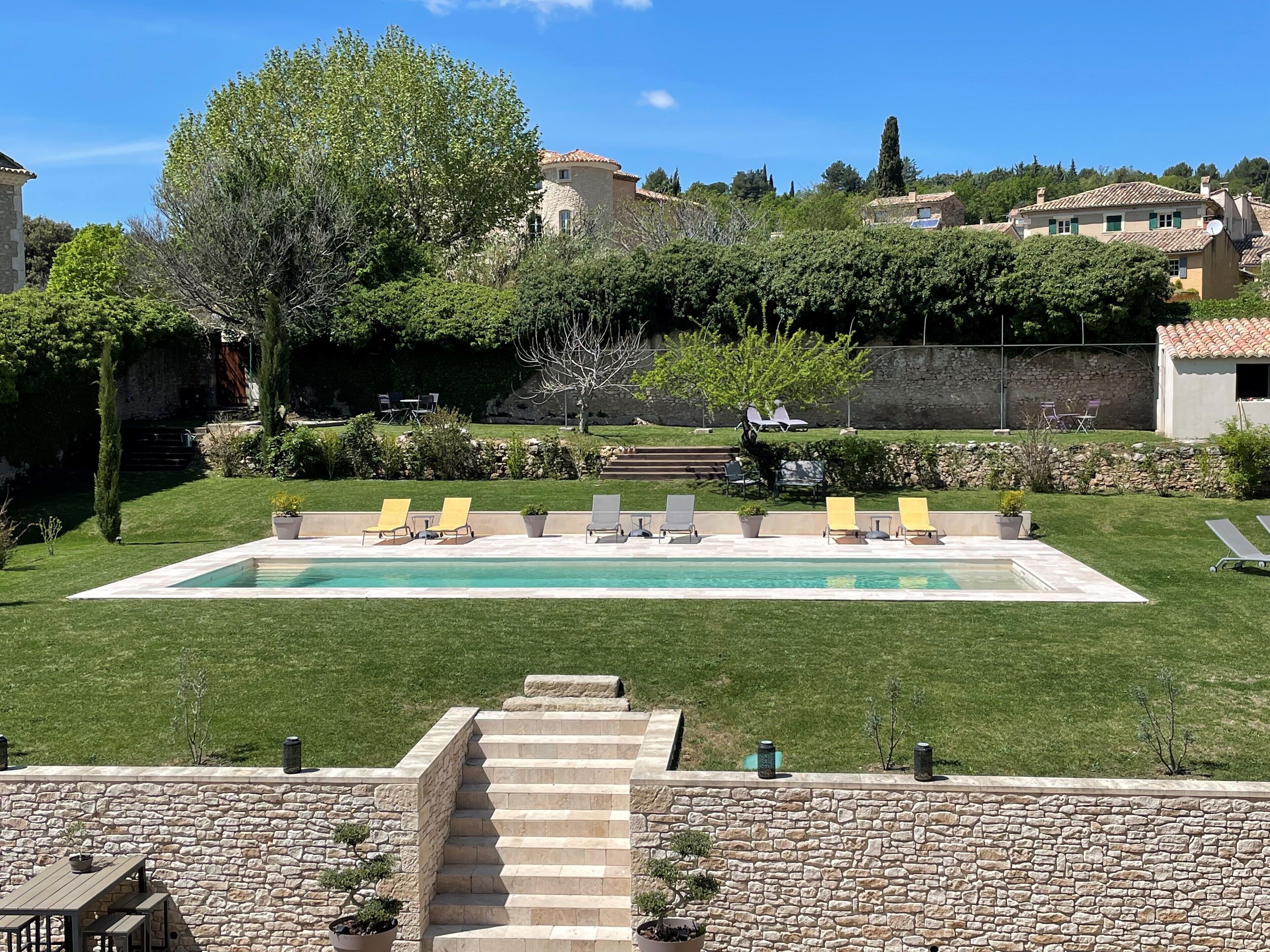 Una piscina con varias sillas de descanso, una escalera de piedra y un muro de piedra.