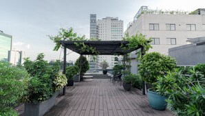 Une terrasse sur le toit agrémentée de plantes en pot, d’une pergola et offrant une vue sur les bâtiments environnants.