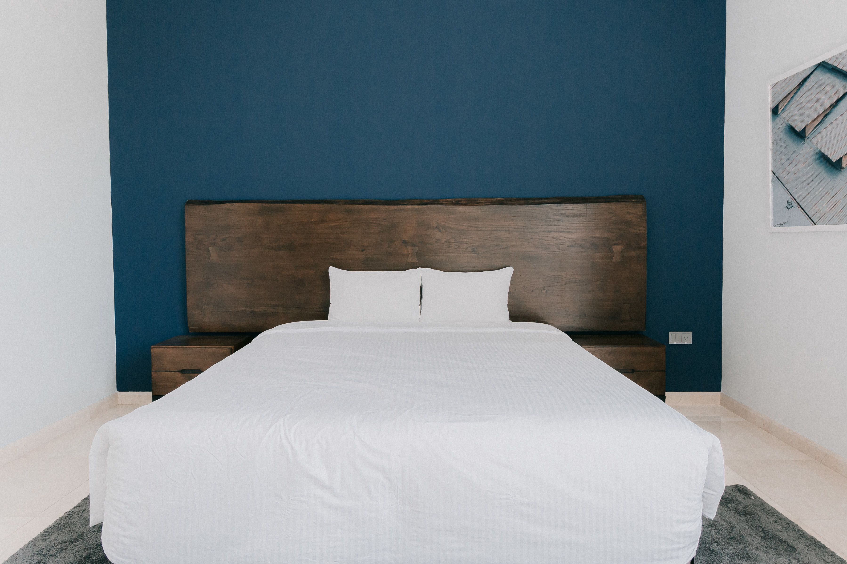 Una cama bien hecha con cabecera de madera en una habitación con pared azul.