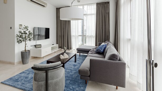 Un salon moderne avec un canapé gris, une table basse, un téléviseur et une grande fenêtre avec des rideaux.