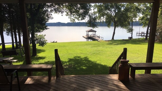 Una terraza de madera con vistas a un lago, un pabellón y una zona ajardinada.