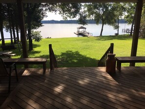 A wooden deck with a view of a lake, a gazebo, and a grassy area.