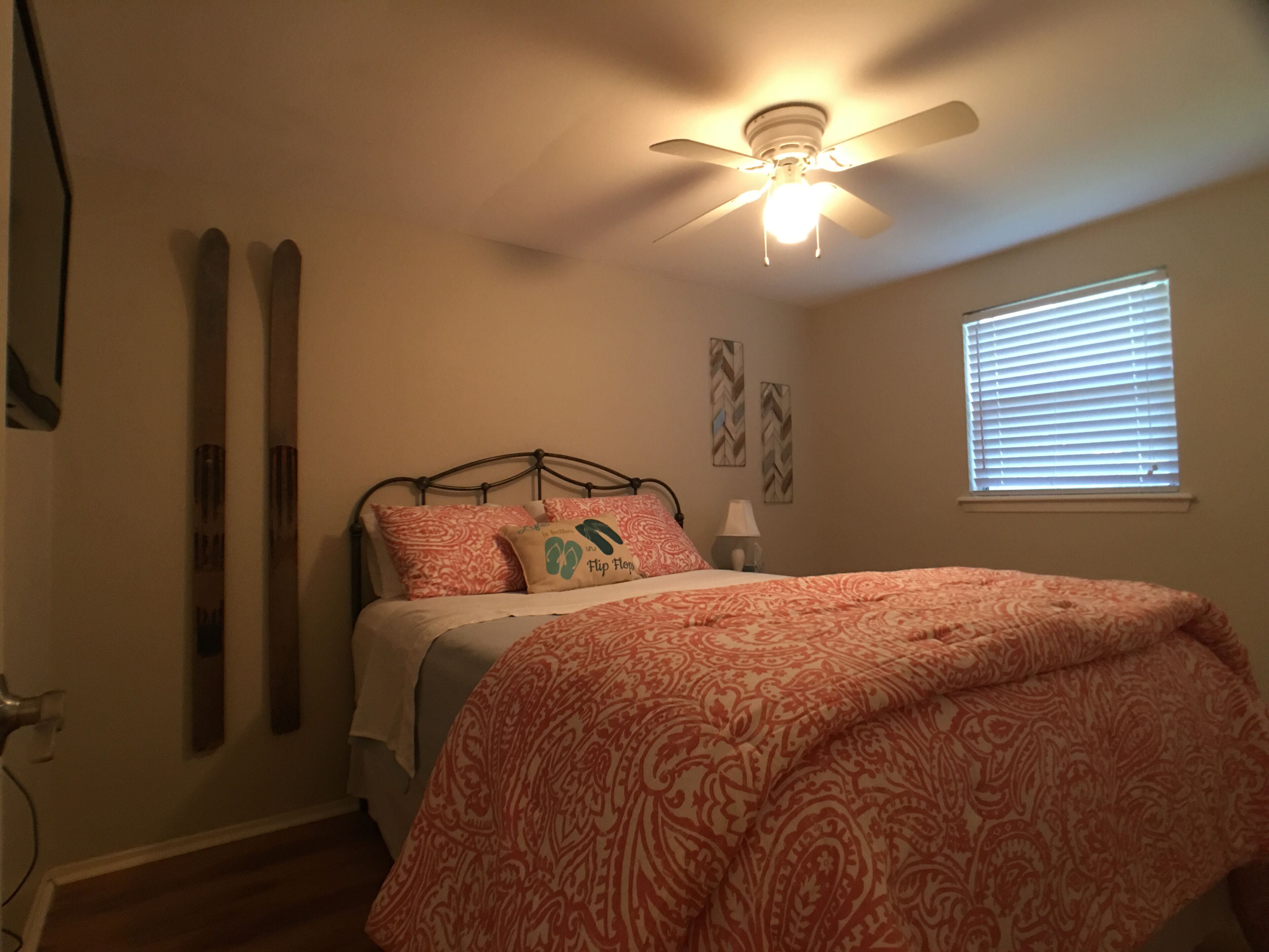 Un dormitorio con cama, ventilador de techo, ventana con persianas y un portaequipajes para esquíes en la pared.