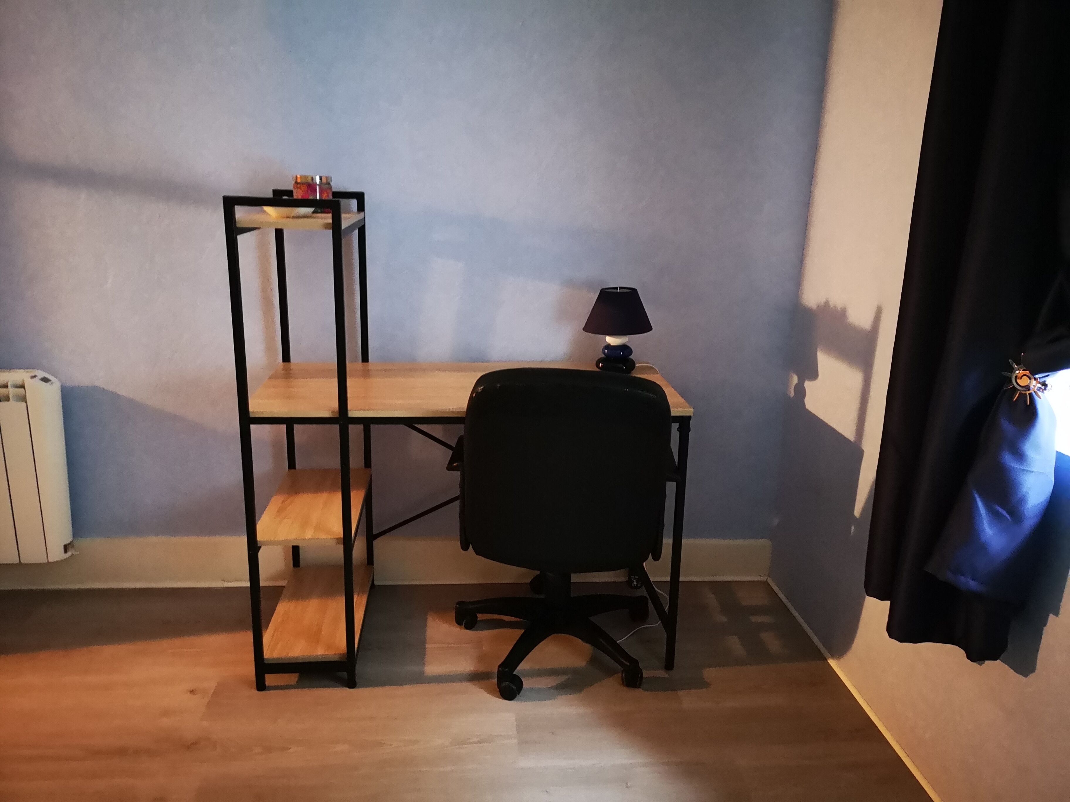 Ein kleiner Büroraum mit Schreibtisch, Stuhl und Regalen.