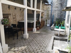 A patio with a brick floor, outdoor seating, a hot tub, and potted plants.