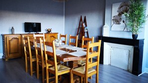 Ruokailutila, jossa on puinen pöytä ja tuolit, televisio, joka on sijoitettu kaappiin, ja ruukussa oleva kasvi.