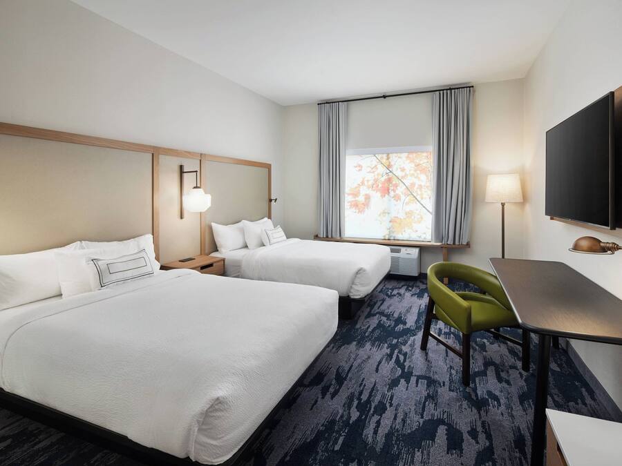 A hotel room with two beds, a desk, a chair, a TV, and a window with curtains.