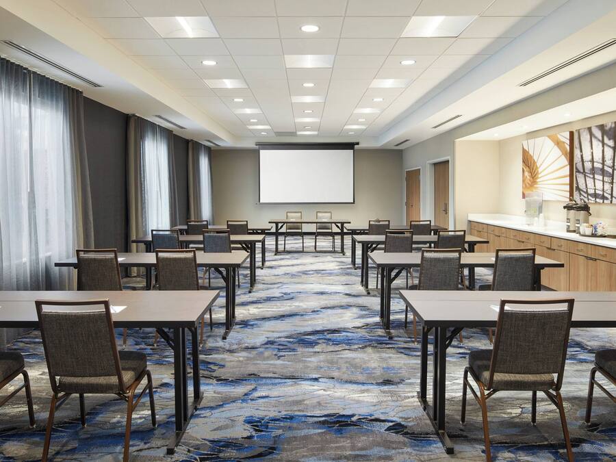 A conference room with a large screen, multiple tables, and chairs arranged for meetings.
