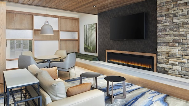 Ein modernes Wohnzimmer mit Kamin, einem flachbildfernseher an einer Steinwand und einer Sitzecke mit Sofa und Sesseln.