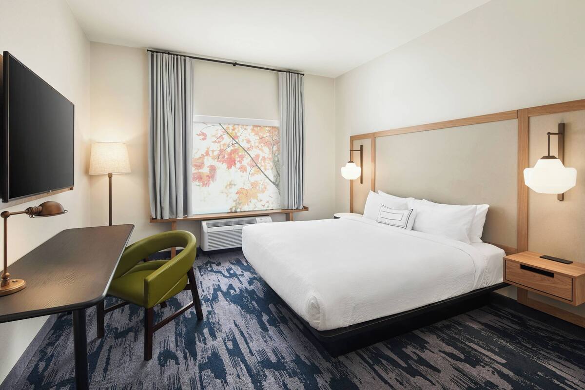 A hotel room with a bed, a desk, a chair, a TV, and a window with curtains.