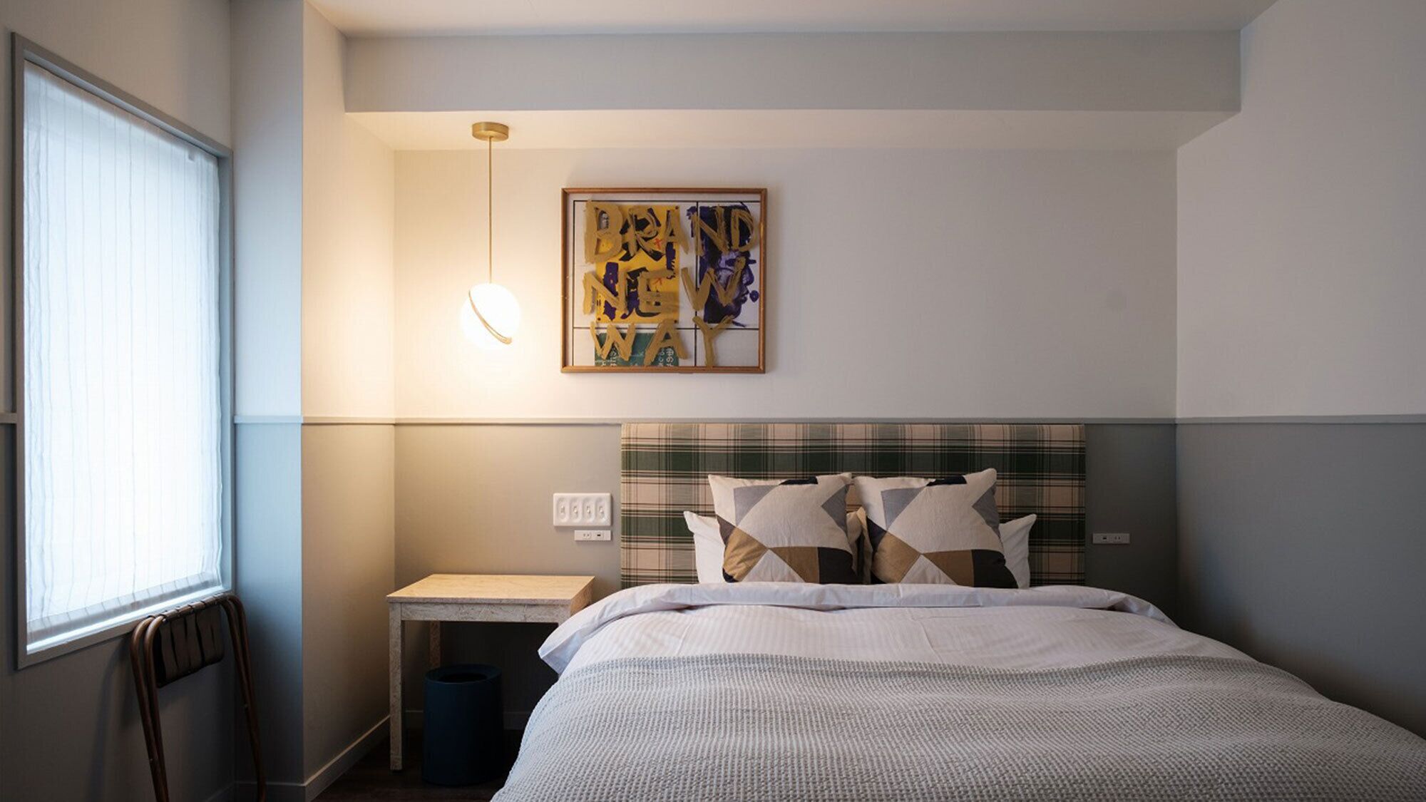 Habitación de hotel con cama, mesita de noche, una obra de arte colgada en la pared y ventana.