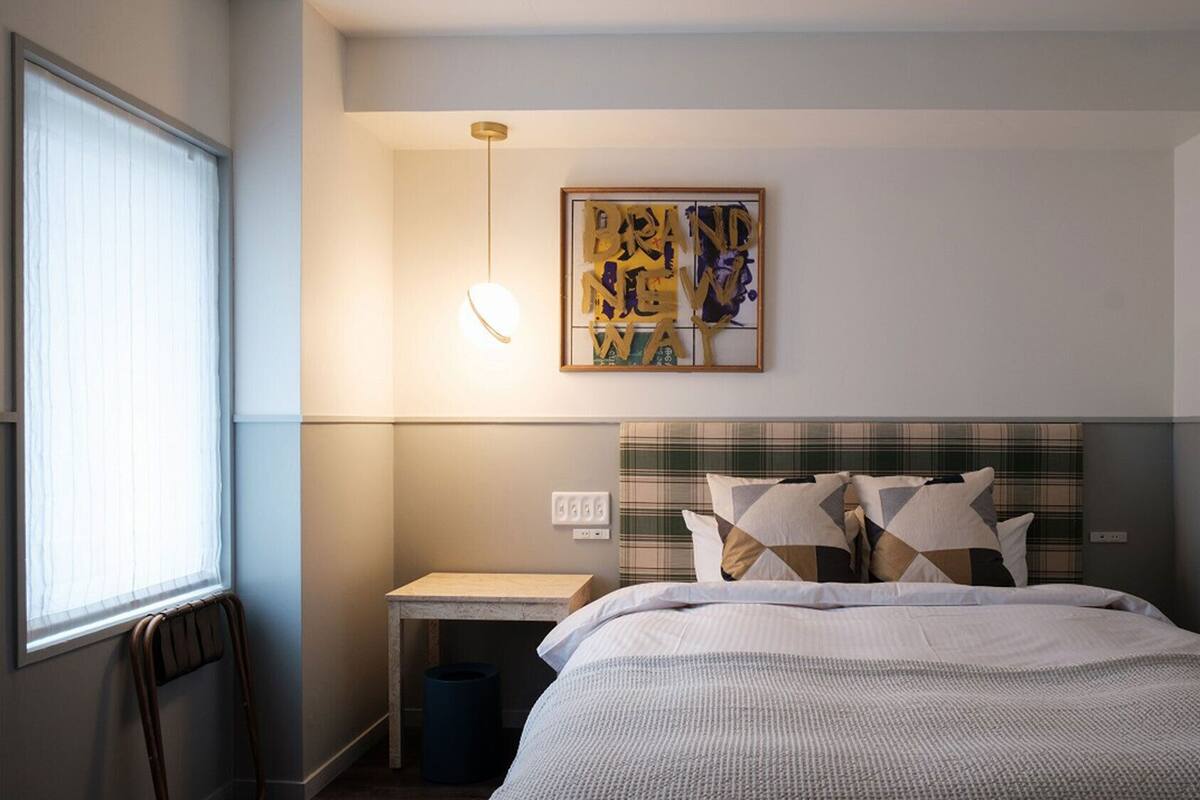 Een hotelkamer met een bed, een nachtkastje, een kunstwerk aan de muur en een raam.